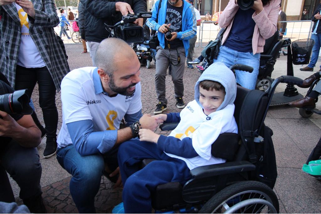 O prefeito Bruno Covas brinca com uma criança cadeirante. Ambos estão sorrindo. 